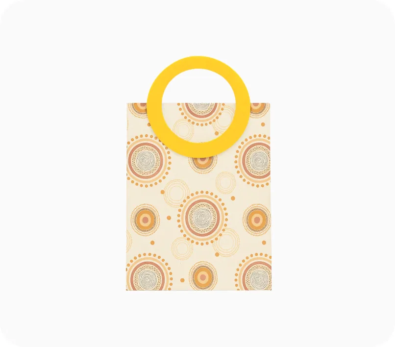 A cream gift bag with a round yellow ring handle, printed with a circular pattern